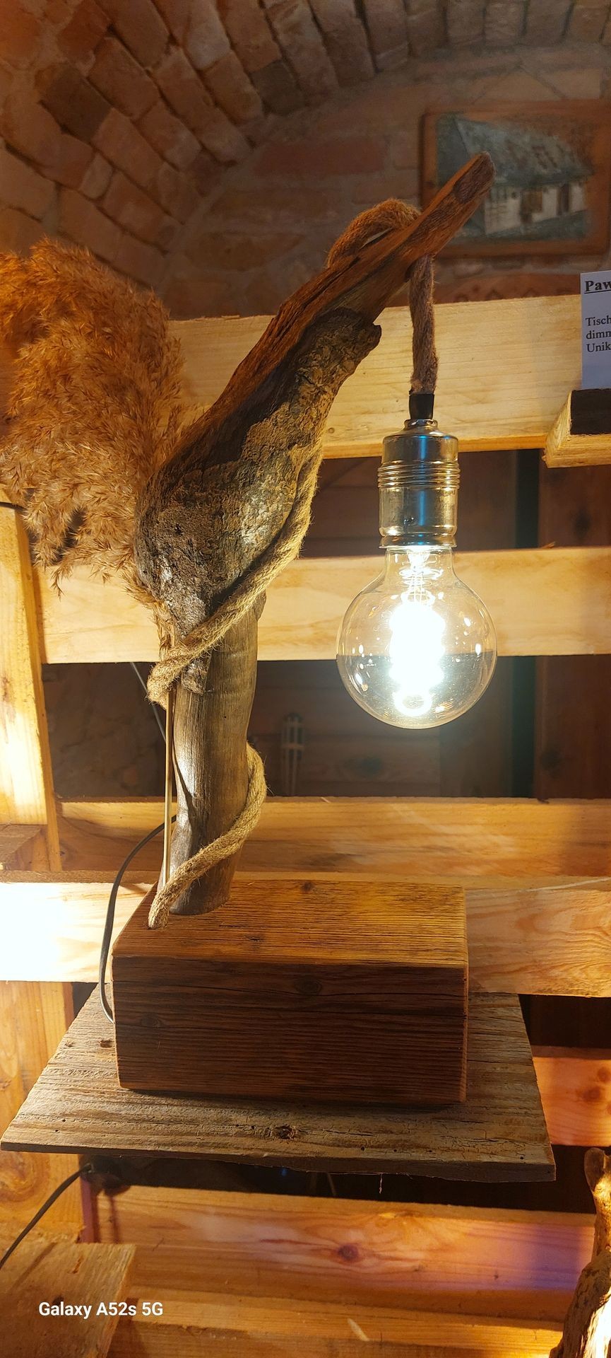 Decorative lamp with exposed bulb on wooden base and rope-wrapped branch.