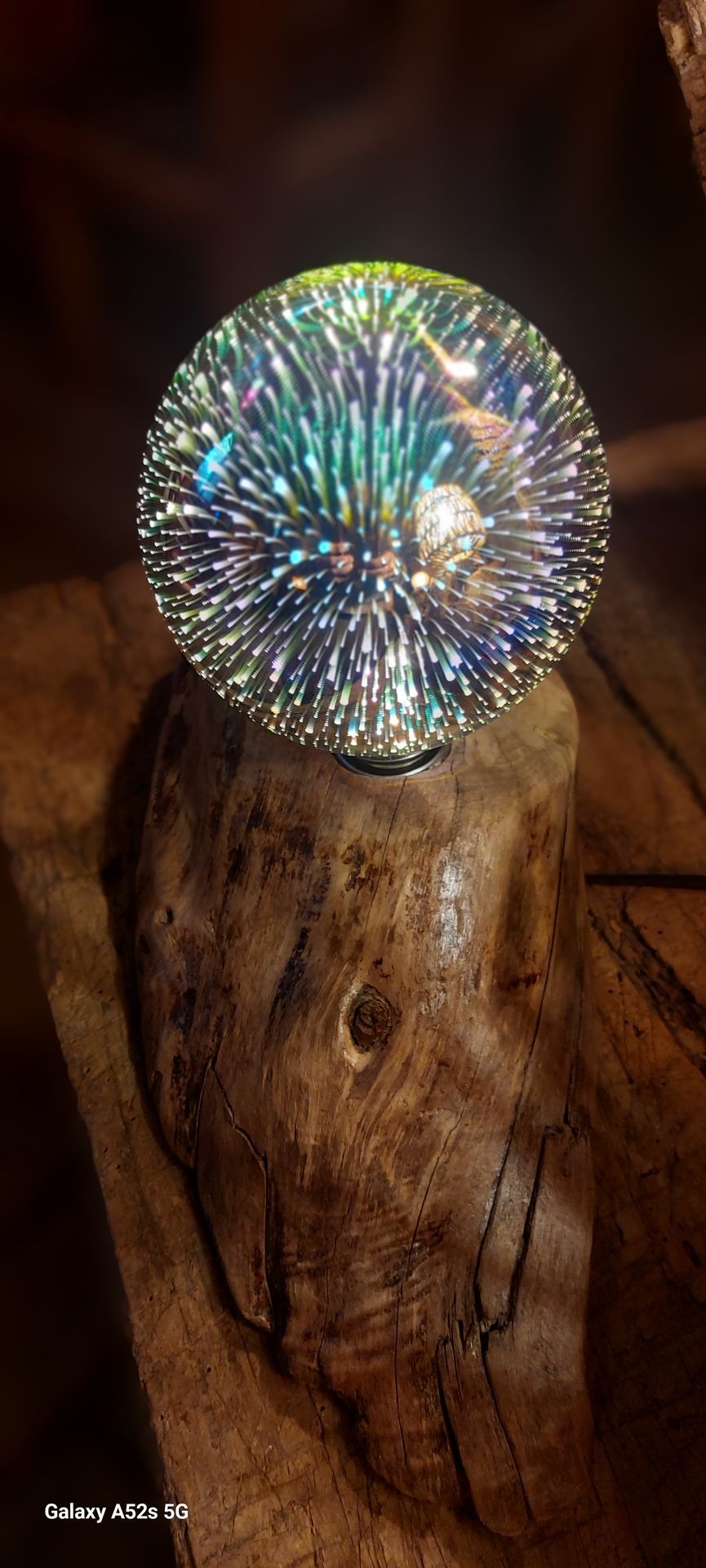 Illuminated spherical light art piece on rustic wooden base, displaying colorful radiant patterns.