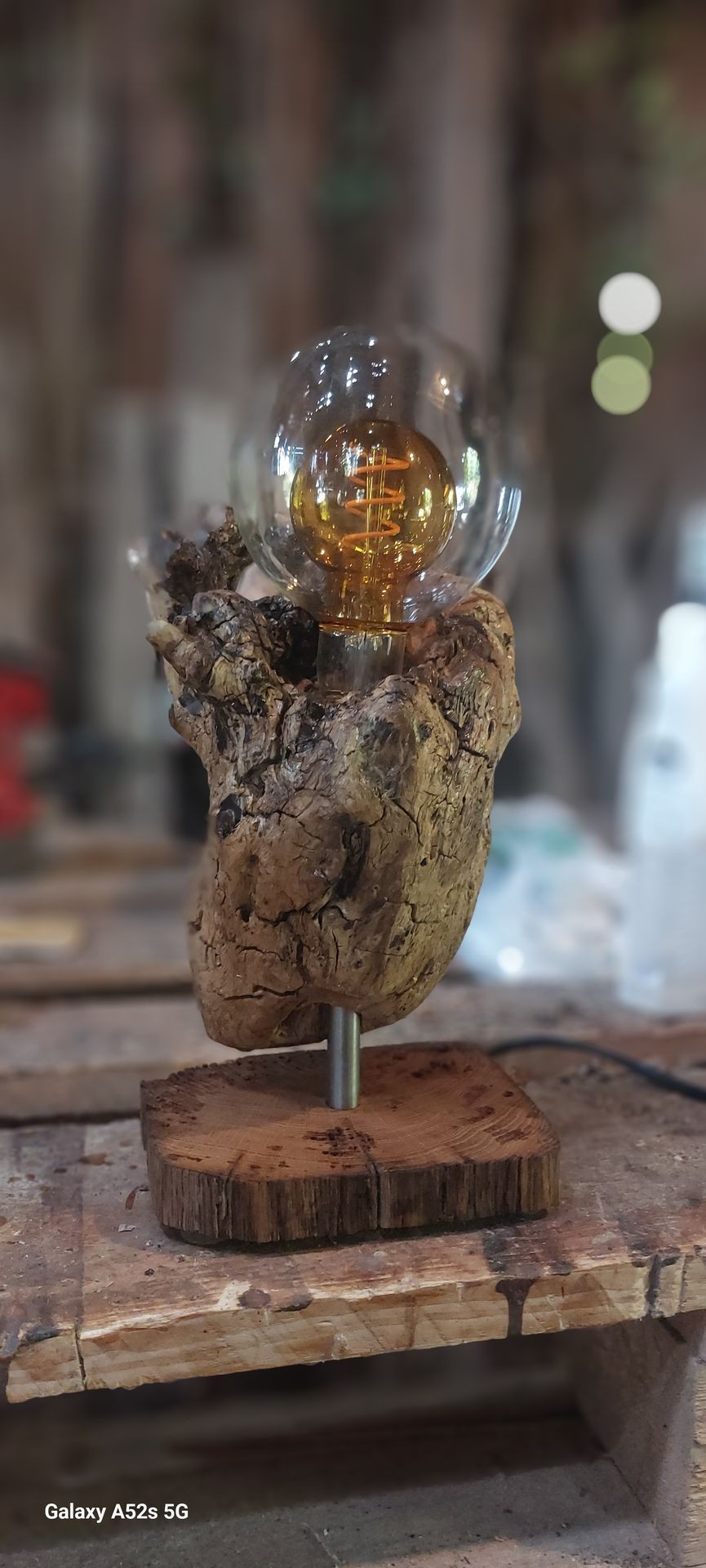 Rustic lamp with clear bulb set on a wooden base, displayed on a workbench.