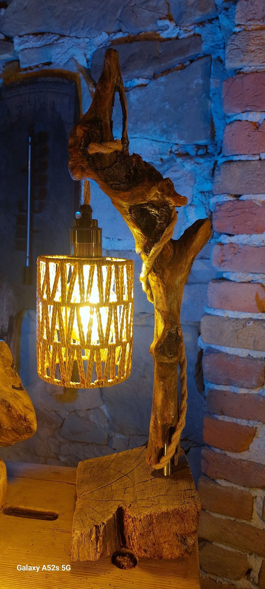 Rustic wooden lamp with a glowing bulb, set against a stone wall background.