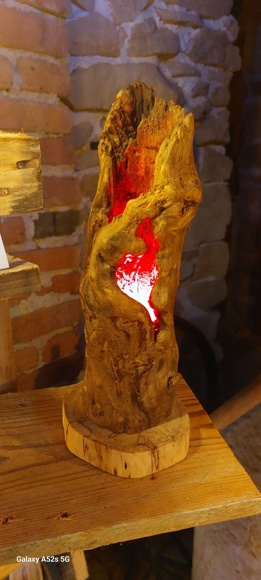 Decorative wooden lamp with red light on a rustic table against a stone wall.