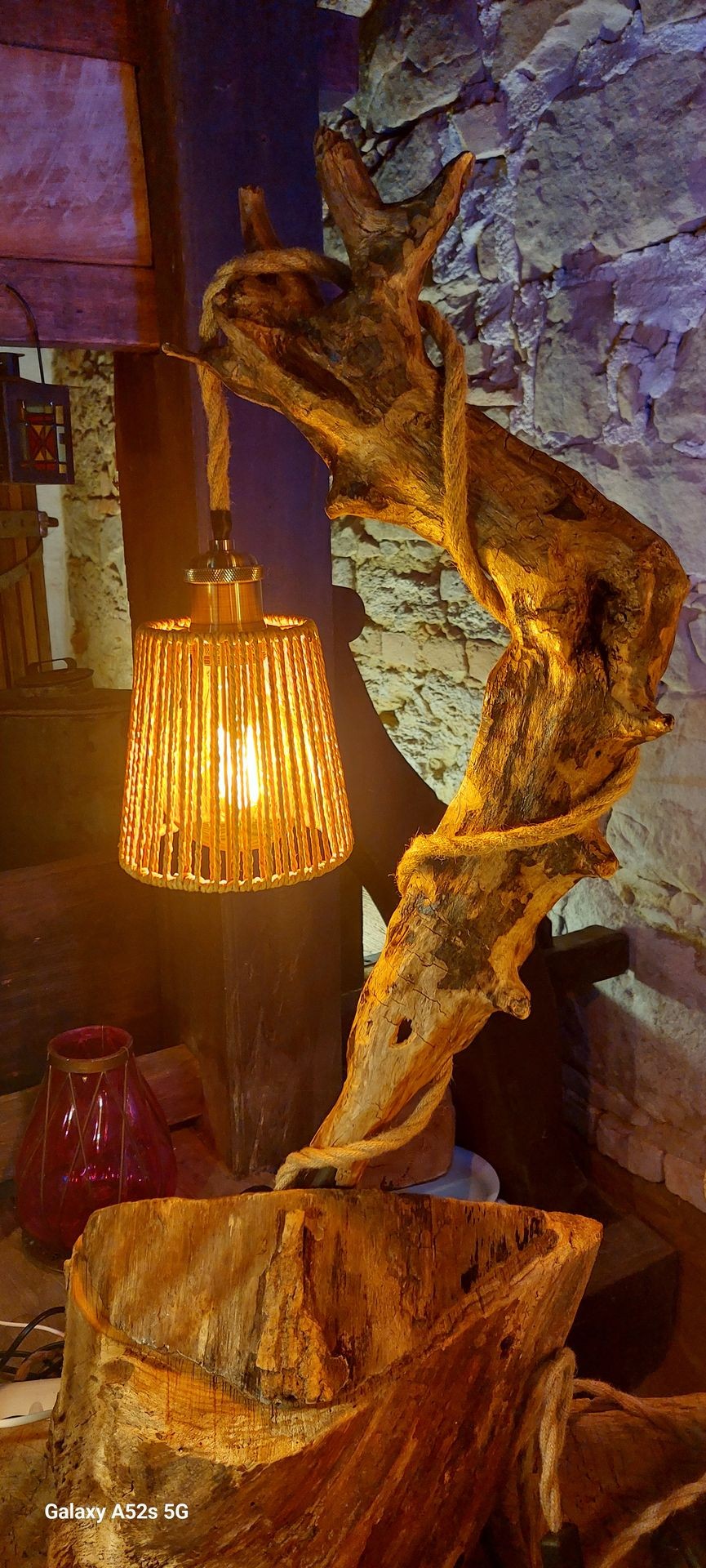 Rustic lantern with warm light hanging from a driftwood sculpture against a stone wall background.