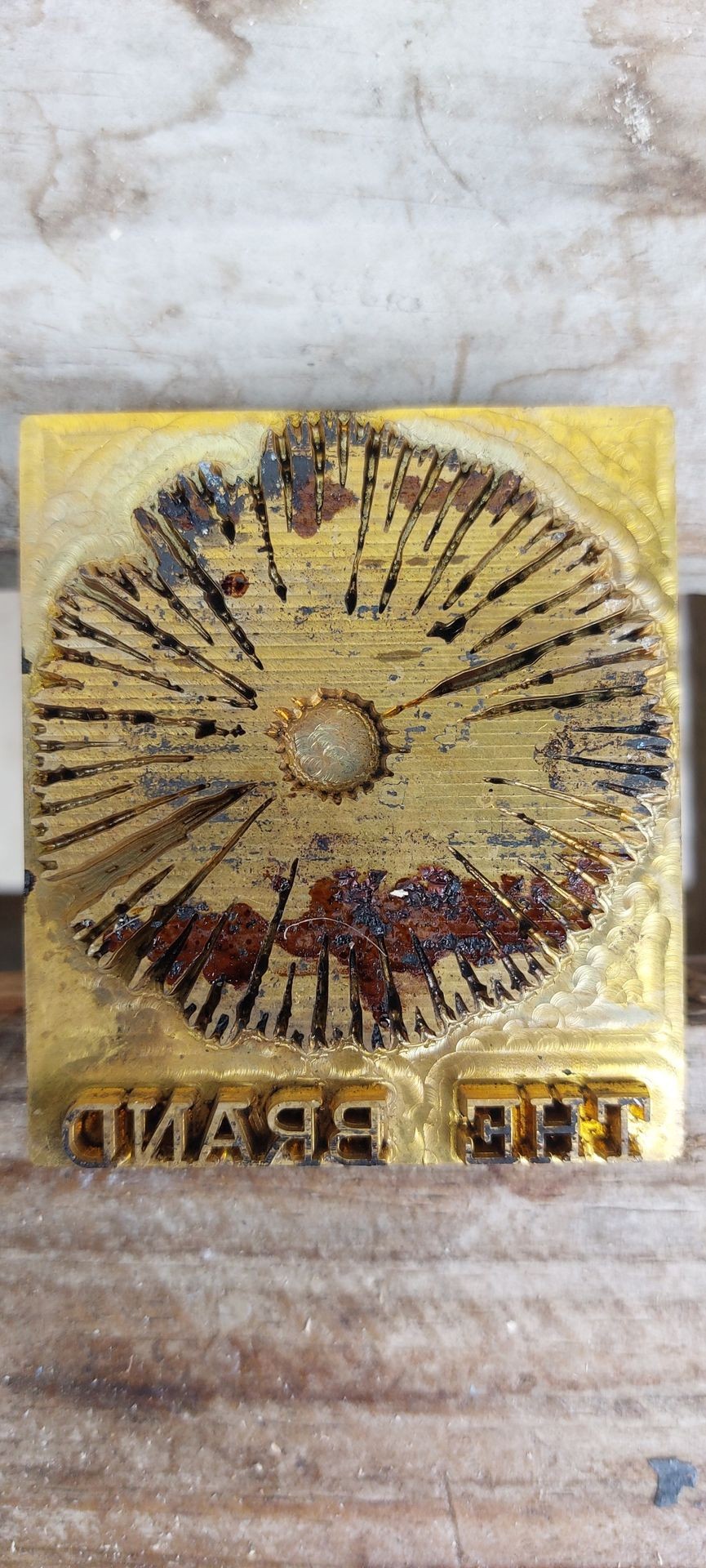 Close-up of a vintage seal on wooden background with engraved radial pattern and letters.