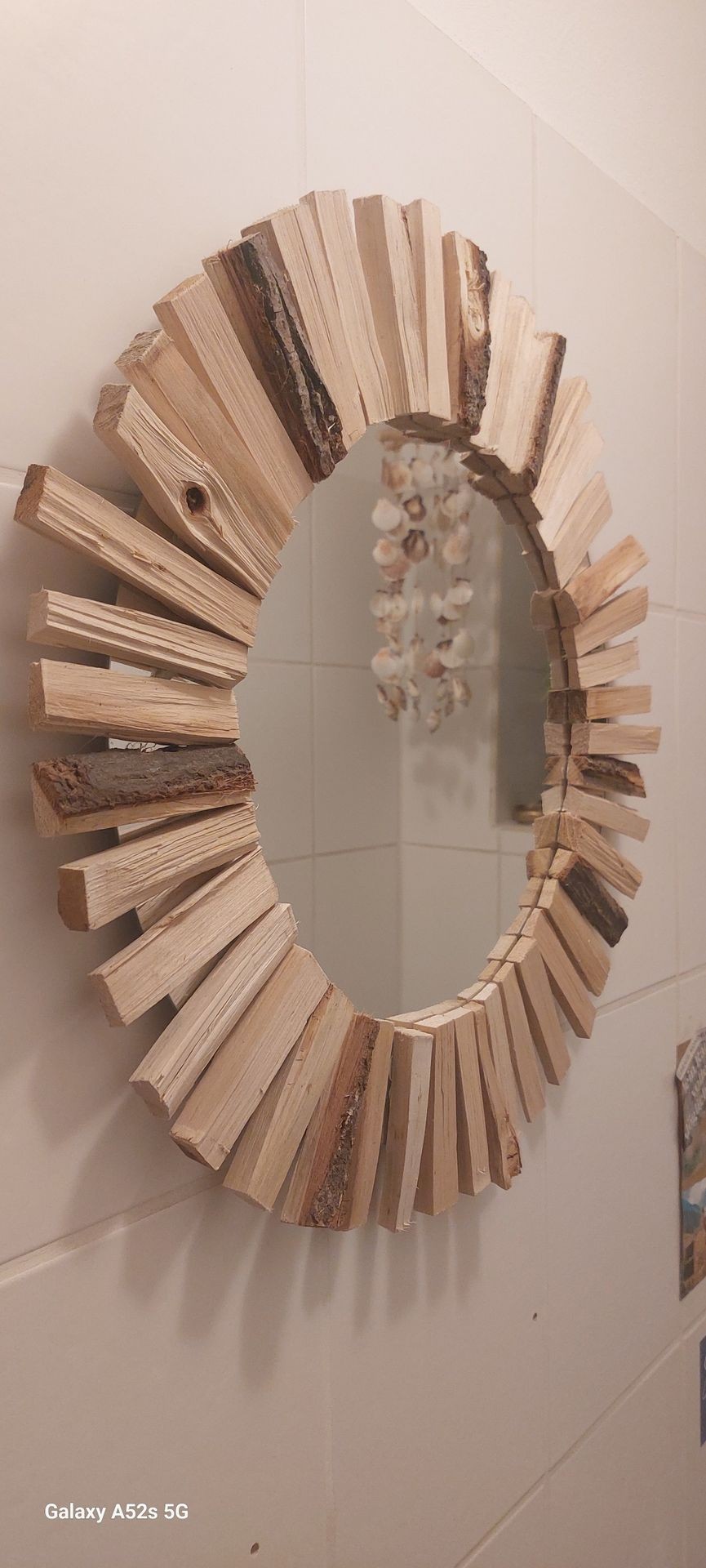 Decorative round mirror with wooden stick frame on a tiled wall.