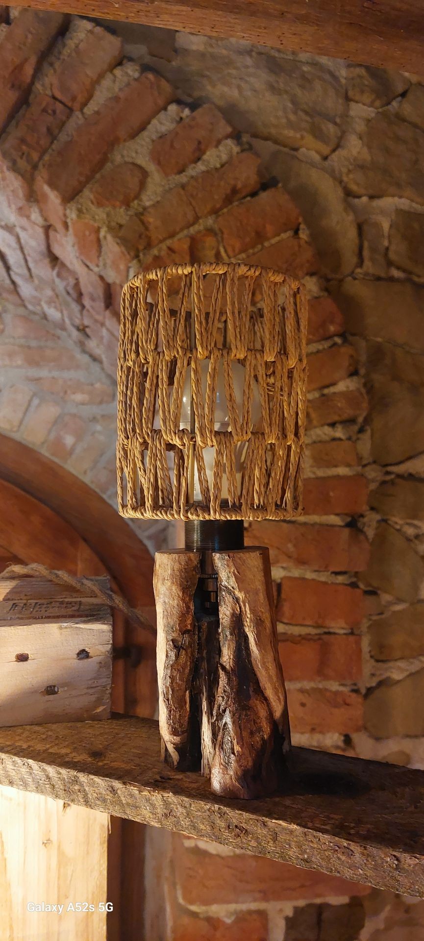 Rustic wooden lamp with woven shade on a brick background.