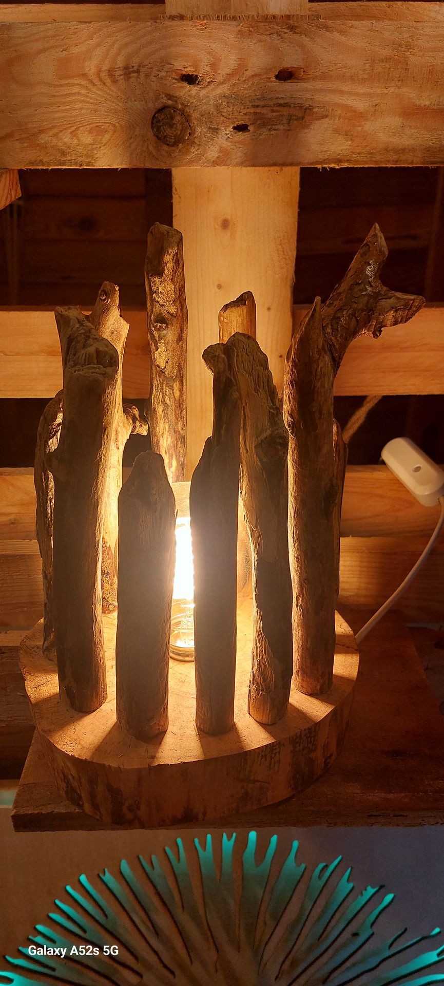 Rustic lamp with wooden branches framing a glowing light bulb on a wooden shelf.