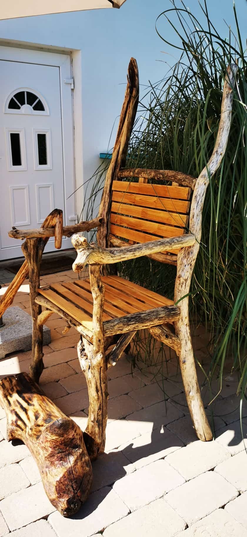 Rustic wooden chair made from natural logs on a stone patio near tall grass.